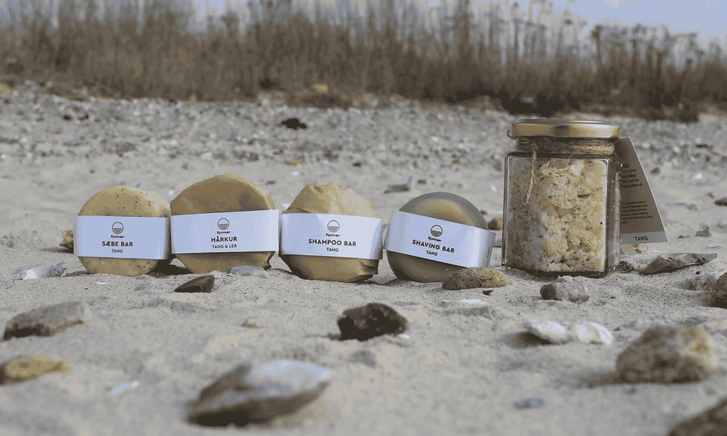 Kystnær sæber, shampoobar, fodbad og saltscrub der ligger på en strand i sandet